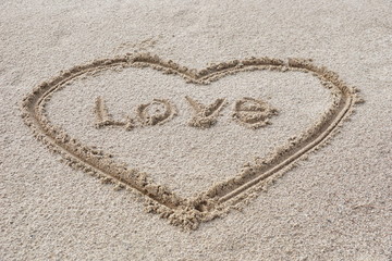 heart drawn on the sand on the beach stick in the center inscription love