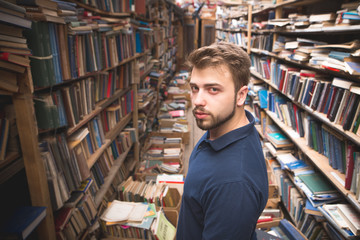 Fototapeta na wymiar Portrait of a man with a beard standing on the background of an atmospheric public library and looking into the camera. Student in a cozy library.