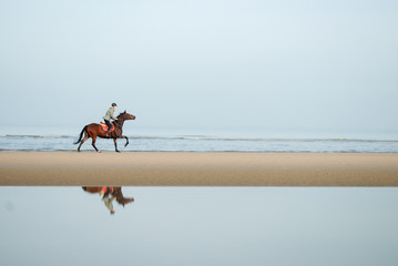 person relaxed horse riding on the beach near the coastline with is reflection in the water