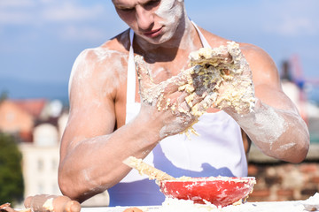 Man muscular baker or cook kneading dough in bowl. Hands of chef cook covered with sticky dough and...