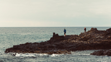 Anglers are fishing on rocky coastline. Tenerife, Spain.