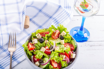 Fresh greek salad served in bowl with glass of white wine.