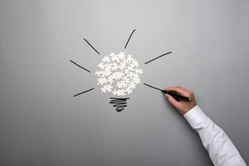 Scattered puzzle pieces and male hand drawing light bulb