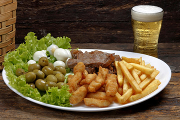 dish with assorted morsels, olive, meat, quail egg, french fries and cold beer