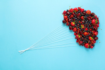 Hand holding balloons made of berries on blue paper background. Healthy eating concept. Flat lay.