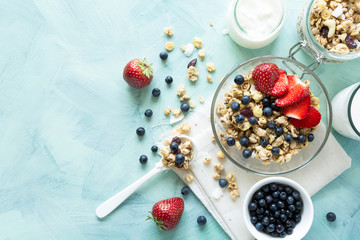 Bowl of homemade granola with strawberry, blueberry, milk and yogurt on turquoise wooden background. Top view. Flat lay. Copy space
