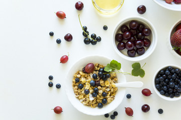 Bowl of homemade granola with strawberry, blueberry, cherry, gooseberry, black currant and honey on white wooden background. Top view. Flat lay. Copy space
