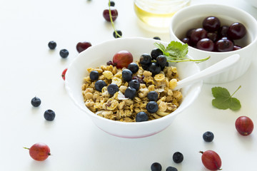 Bowl of homemade granola with strawberry, blueberry, cherry, gooseberry, black currant and honey on white wooden background. Top view. Flat lay. Copy space