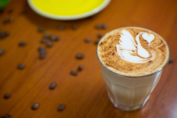 a glass of coffee with swan latter art and coffee bean on wood table