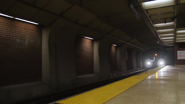 Subway train with headlights arrives from dark tunnel at empty station platform