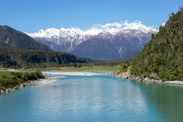 New Zealand scenery, mountains with snow on the top with turquoises riverfront in forest and blue sky in background