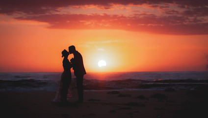 silhouette of couple lovers, bride and groom holding hands during sunrise time at the beach with beautiful pink sunrise sky.