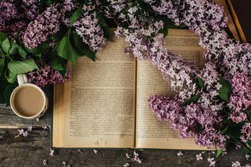 Cup of tea, lilac flowers, book on dark wooden background