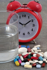 Verre d'eau à côté de médicaments et d'un réveil-matin