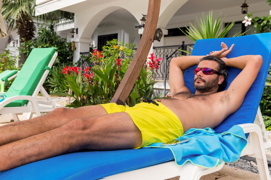 Bearded Caucasian man with sunglasses resting on a sunbed in a resort