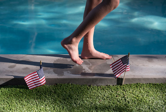 Boy walking along the edge of a swimming pool and American flags