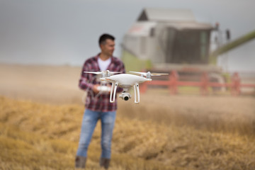 Farmer driving drone above wheat field during harvest - obrazy, fototapety, plakaty