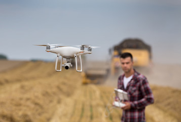 Farmer driving drone above wheat field during harvest - obrazy, fototapety, plakaty