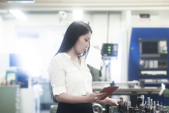 Female engineer standing in a workshop holding a digital tablet and selecting drill bits