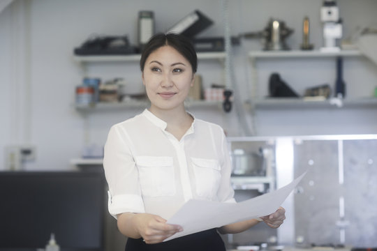 Smiling Female engineer standing in a workshop looking at technical drawings