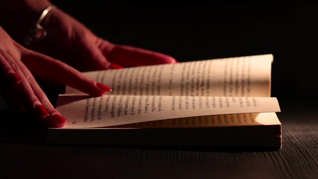 Mano di Donna sfoglia un Libro con Luce Calda. Scena Notturna
