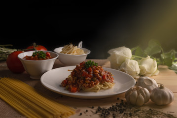 Delicious spaghetti with various spices, garlic, pepper, oregano, parsley and white roses on isolated black background.