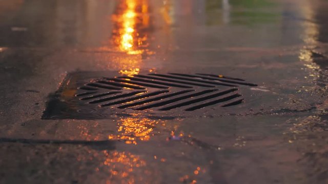 Rain falling in slow motion down a sewer drain at night in the city.
