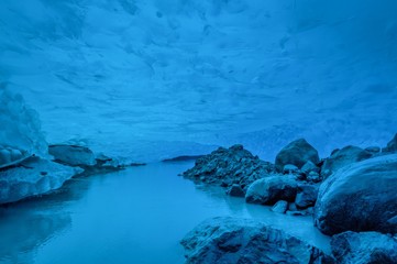 Melted glacier flows through an ice cave under Perito Moreno Glacier, El Calafate, Argentina. Sunlight penetrates through the glacier and cast a hue of blue and turquoise on textured ice surface.