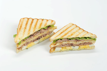 Two sandwiches of triangular shape made of white bread. The filling of the sandwich consists of pieces of tuna, hard boiled eggs, lettuce leaves, pieces of cheese and sauce. Closeup. White background.