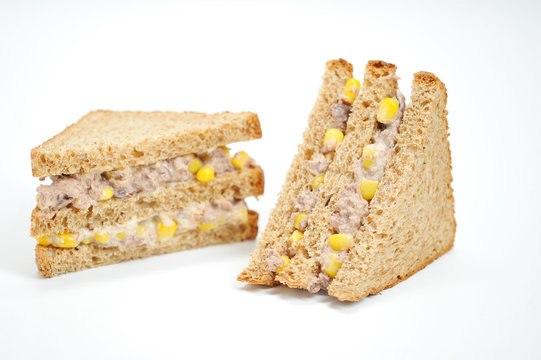 Two sandwiches of a triangular shape on a white background. The filling of the sandwich consists of corn and tuna. Close-up.