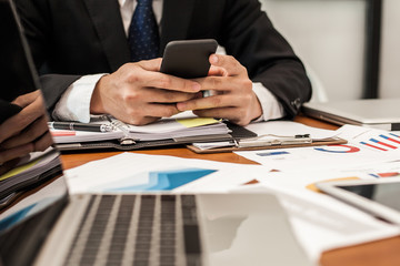 A businessman analyzing investment charts at workplace and using laptop and touch tablet.