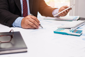 A man's hand holding pen pointing on summary report chart and calculate finance in office.