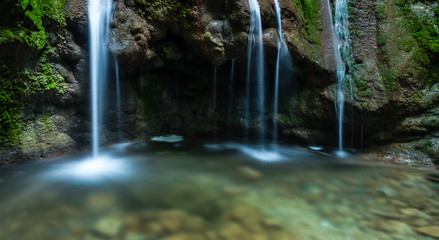 Fototapeta premium Long exposure small creek waterfall, silver water streams flow down on stones covered with green moss in cold river
