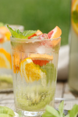citrus lemonade in glass jug with mint. Orange. Grapefruit and lemon. On greenery background.