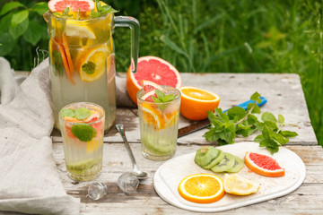 citrus lemonade in glass jug with mint. Orange. Grapefruit and lemon. On greenery background.