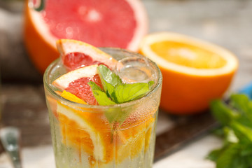 citrus lemonade in glass jug with mint. Orange. Grapefruit and lemon. On greenery background.