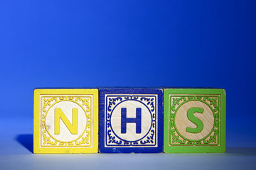 Wooden letter blocks on a blue background spelling out the initials NHS