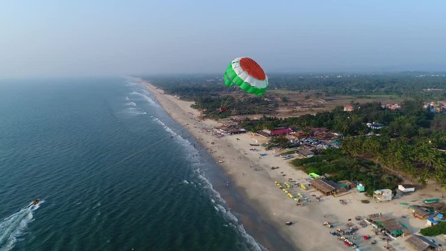 Colored parachute behind a motorboat over the sea and landing on the beach. Fun for tourists on sunset. Aerial view.