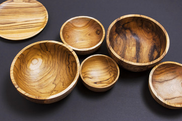 Wooden utensils for the kitchen, bowls, plates on a black background. The concept of natural dishes, a healthy lifestyle. Texture of wood. Wooden eco-ware
