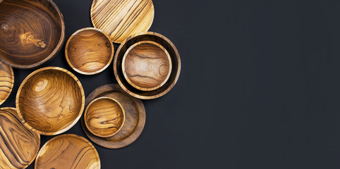 Wooden utensils for the kitchen, bowls, plates on a black background. The concept of natural dishes, a healthy lifestyle. Texture of wood. Wooden eco-ware