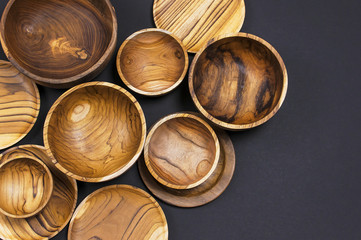 Wooden utensils for the kitchen, bowls, plates on a black background. The concept of natural dishes, a healthy lifestyle. Texture of wood. Wooden eco-ware