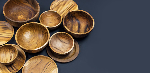 Wooden utensils for the kitchen, bowls, plates on a black background. The concept of natural dishes, a healthy lifestyle. Texture of wood. Wooden eco-ware