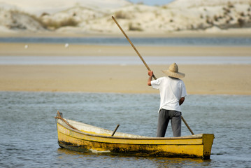 barqueiro de costas atravessando com barco amarelo o rio e dunas de areia branco ao fundo