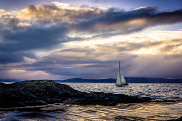Sailboat among the rocks against the background of a spectacular sunset.