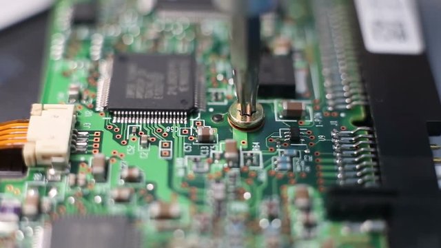 Closeup of a hand which unscrew the screw on circuit board.