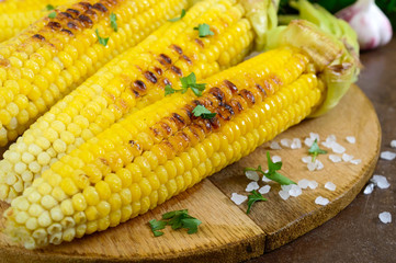 Fresh tasty grilled sweet corn with butter, sea salt and cilantro on a wooden table. Summer dinner or snack. Ideas for barbecue and grill parties. Vegetarian, healthy diet concept.