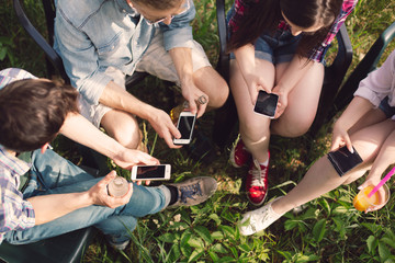 Top shot of young people with their phones sitting in circle. Group of friends sittting outdoors on picnic using their phones instead of talking to each other.