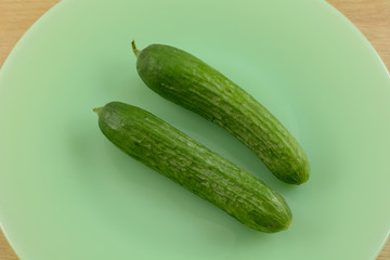 Two raw whole Persian cucumbers or Cucumis sativus on green plate