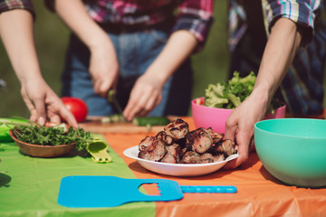Close up shot of friends cooking together for lunch outdoors. Group of people preparing some food on picnic table outdoors with meat vegetables and herbs.