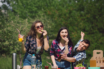 Three friends enjoying food on picnic. Happy young adults having some snacks and drinks on nice day outside on picnic.